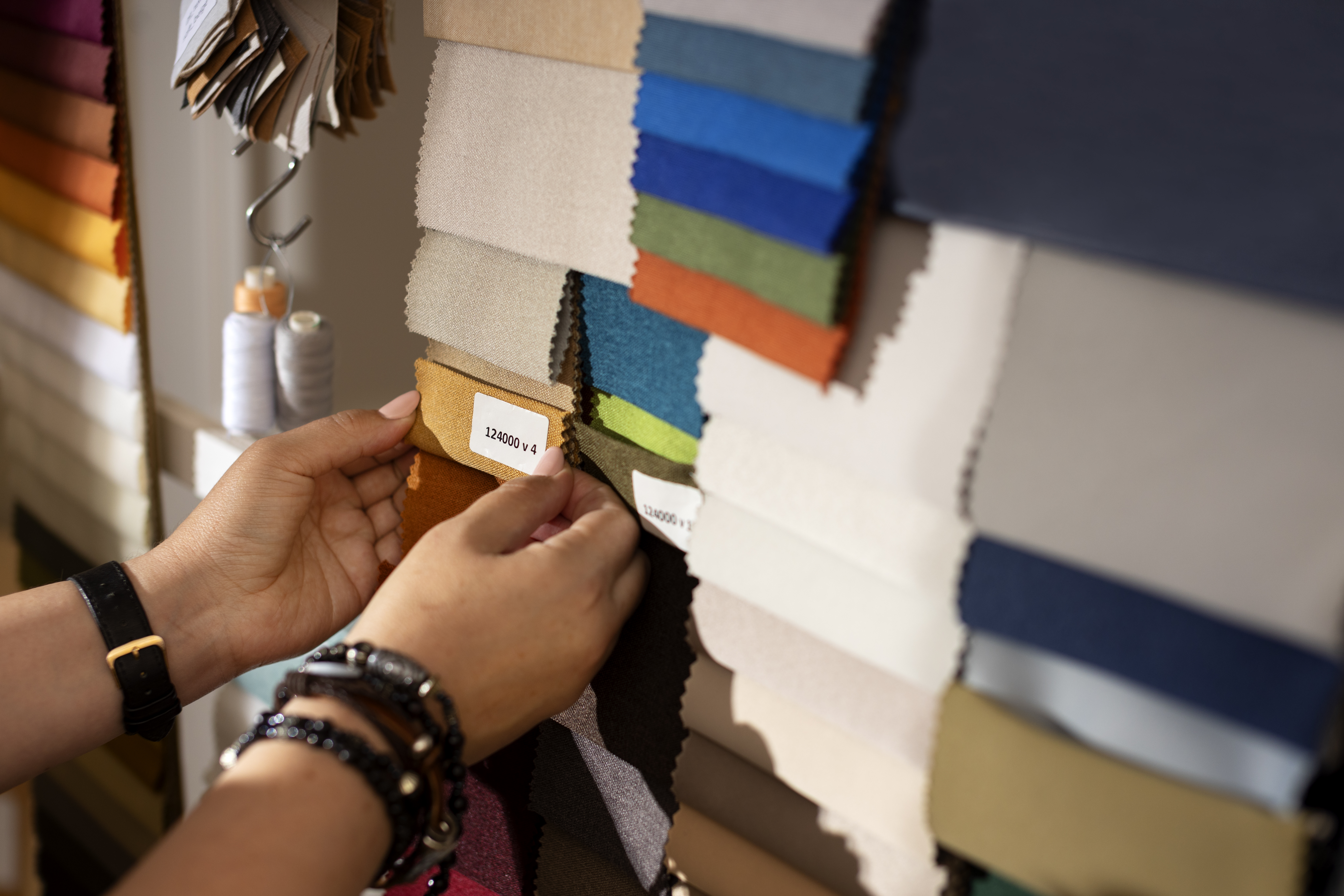Hands sorting through hanging fabric swatch books in a designer's office, comparing colors and weights.
