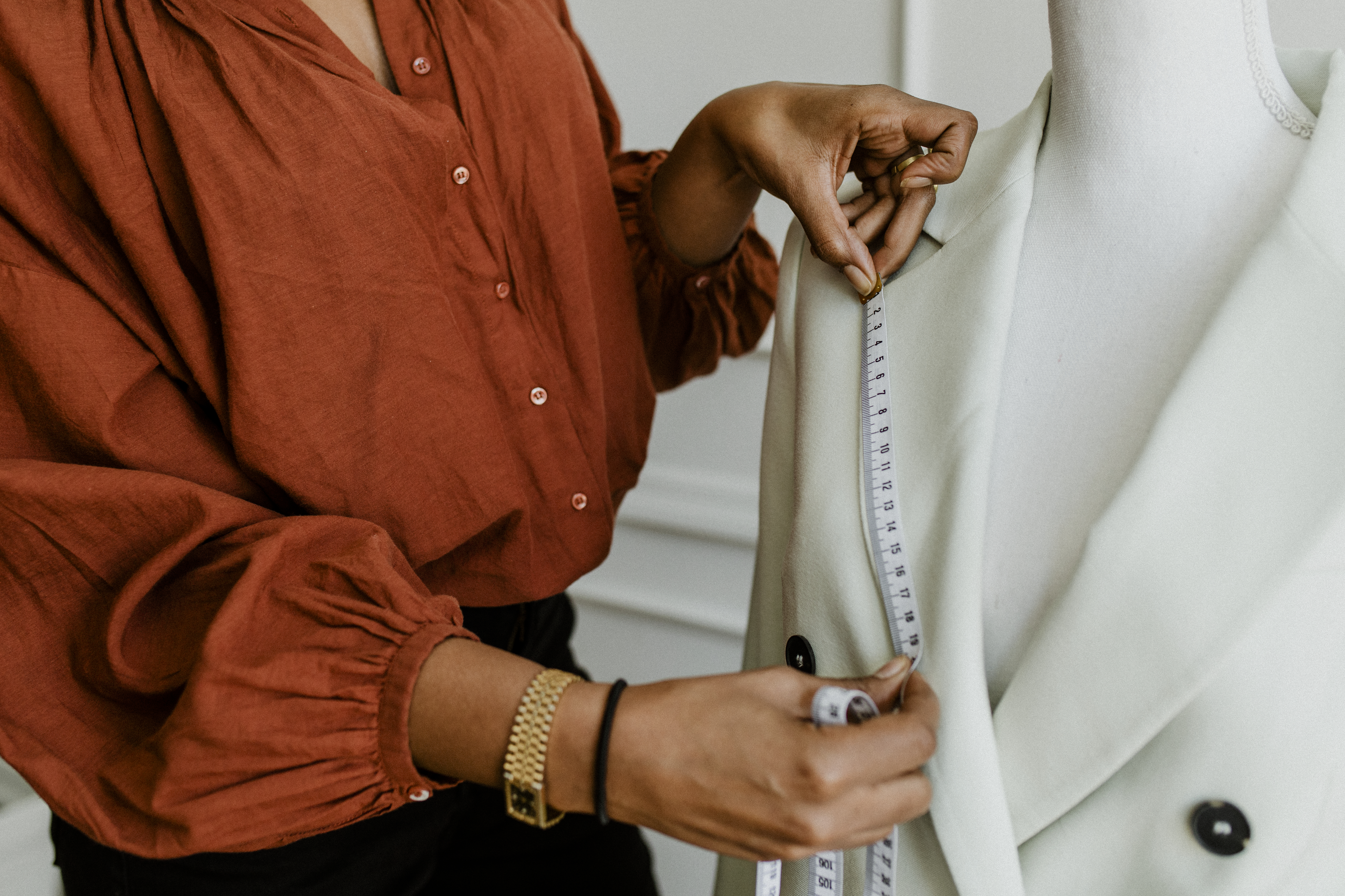 Designer measuring the lapel of a cream blazer on a dress form with a tape measure for a fit revision.