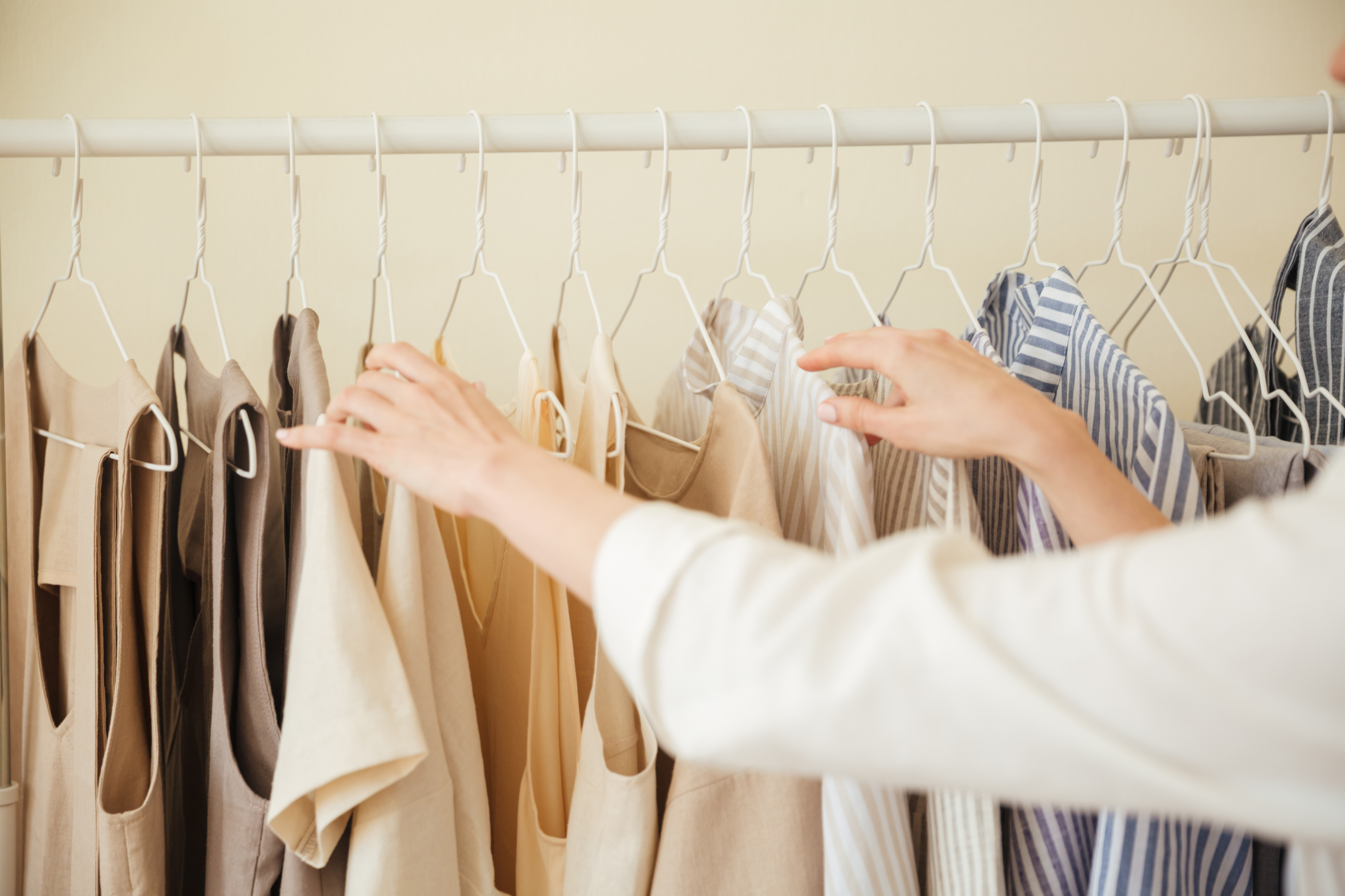 A woman's hands flipping through neutral-toned garments on a workshop clothing rack.
